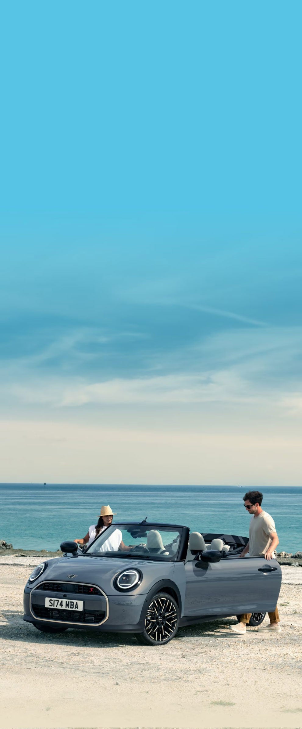 Convertible parked on a beach with two drivers getting into it.