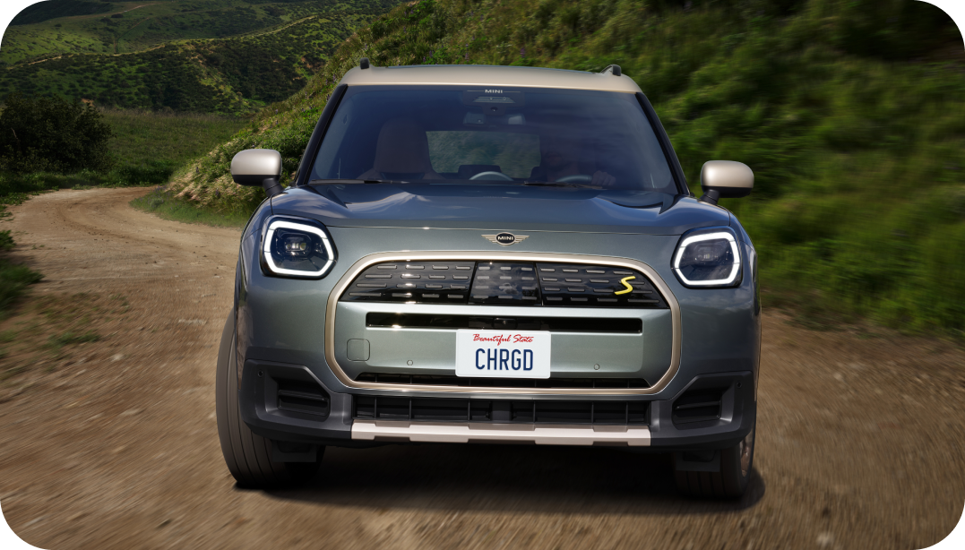 Front-view of a 2025 MINI Countryman SE ALL4 driving up a dirt road in a mountainous region. 